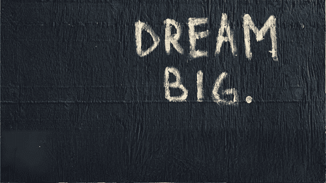 White text reading DREAM BIG. is painted in capital letters on a black textured wall.
