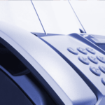 Close-up of a fax machine with paper inserted, showing its keypad and control panel. The image has a blue tint and focuses on the device’s buttons and curved edges.