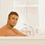 A man with short dark hair sits relaxed in a white bathtub, looking at the camera. The bathroom is bright with white curtains and a classic-style faucet next to him.