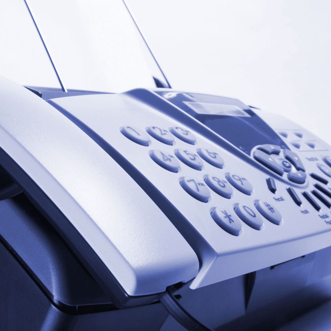 Close-up of a fax machine with visible buttons and paper being fed into the top, photographed in a cool blue-toned light.