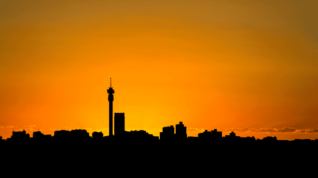 Silhouette of a city skyline with a tall tower at sunset, featuring an orange sky that gradually fades into yellow near the horizon.