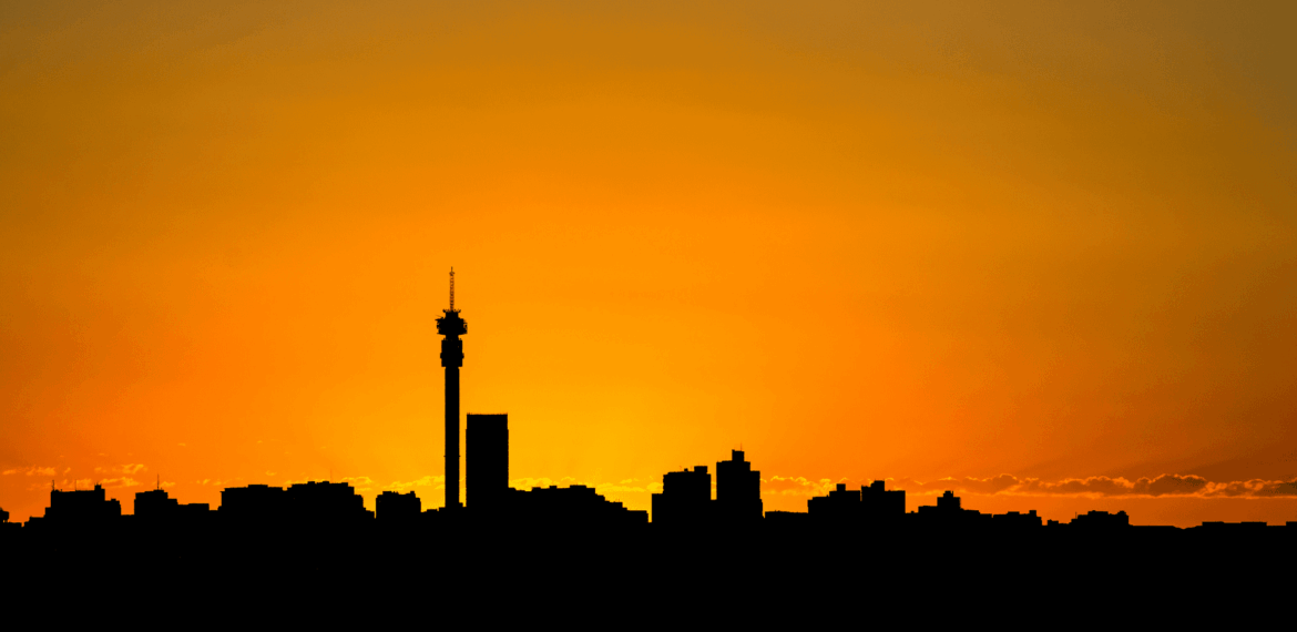 Silhouette of a city skyline with a tall tower at sunset, featuring an orange sky that gradually fades into yellow near the horizon.