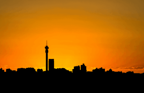 Silhouette of a city skyline with a tall tower at sunset, featuring an orange sky that gradually fades into yellow near the horizon.