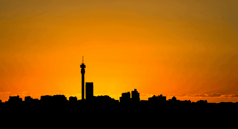 Silhouette of a city skyline with a tall tower at sunset, featuring an orange sky that gradually fades into yellow near the horizon.