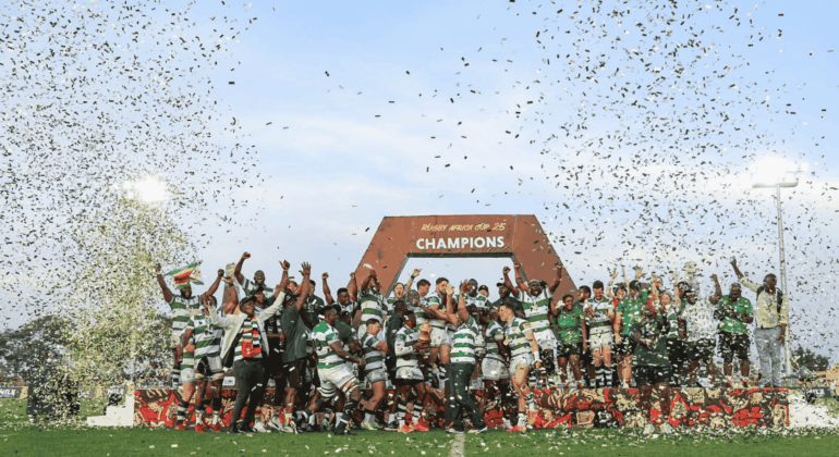 A rugby team celebrates winning a championship on a field, standing under a large CHAMPIONS sign while confetti falls around them. Players and coaches raise their hands in victory and joy.