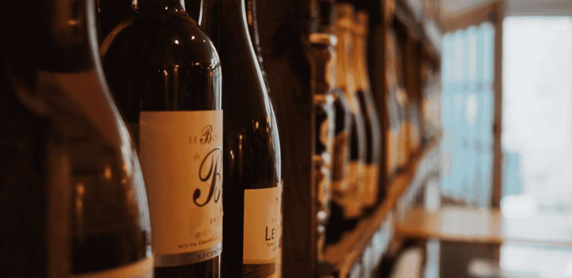 Close-up of wine bottles on a shelf in a dimly lit store or wine shop, with blurred shelves and a door visible in the background.