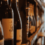 Close-up of wine bottles on a shelf in a dimly lit store or wine shop, with blurred shelves and a door visible in the background.