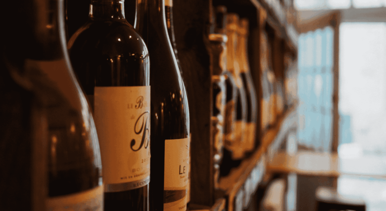 Close-up of wine bottles on a shelf in a dimly lit store or wine shop, with blurred shelves and a door visible in the background.