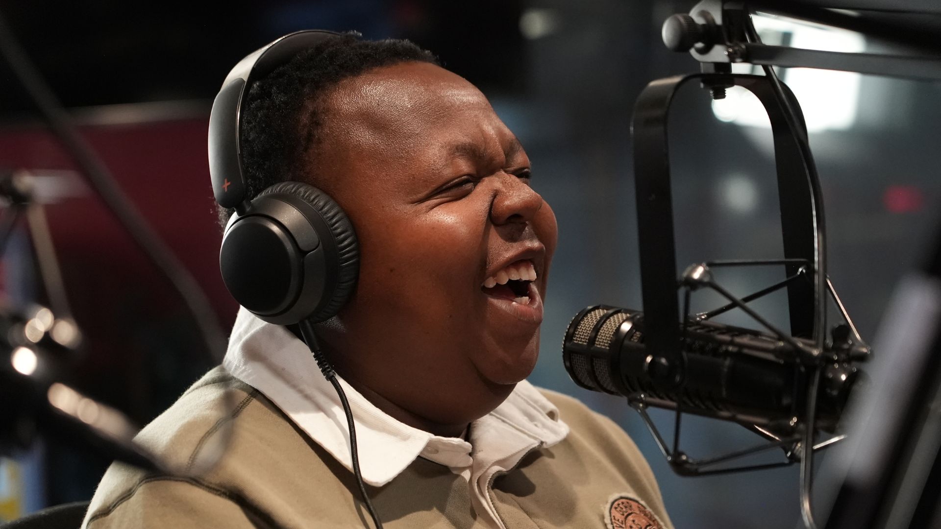 A person wearing headphones and speaking into a microphone laughs while recording in a professional radio studio, joking about the surprising uses of vinegar.