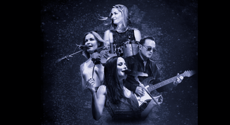 Four musicians perform on stage, reminiscent of The Corrs: three women singing while playing violin, drums, and guitar, with a man on electric guitar—all set against a starry, dark blue background.