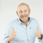 A smiling bald man wearing a light blue button-up shirt gives two thumbs up against a plain light background, showing he's clearly free from any brainrot.