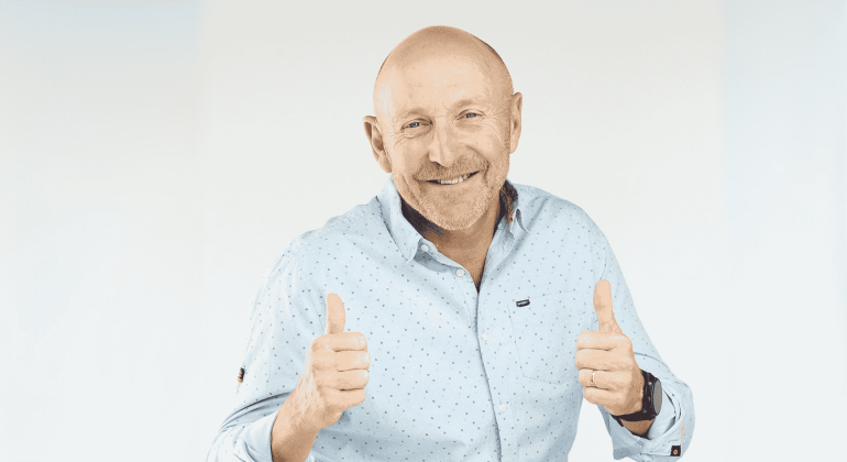A smiling bald man wearing a light blue button-up shirt gives two thumbs up against a plain light background, showing he's clearly free from any brainrot.