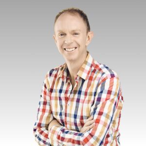 A smiling person in a colorful plaid shirt stands with arms crossed against a light gray gradient background.