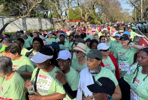 A large crowd of women in light green SPAR t-shirts and race bibs gathers outdoors for the SPAR Women’s Challenge, ready for a running or walking event on a sunny day, surrounded by trees and greenery.
