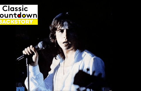 A young man with long hair wearing a white shirt holds a microphone and sings on stage against a dark, blurred background. The Classic Countdown Backstory logo appears in the top left corner of the image.
