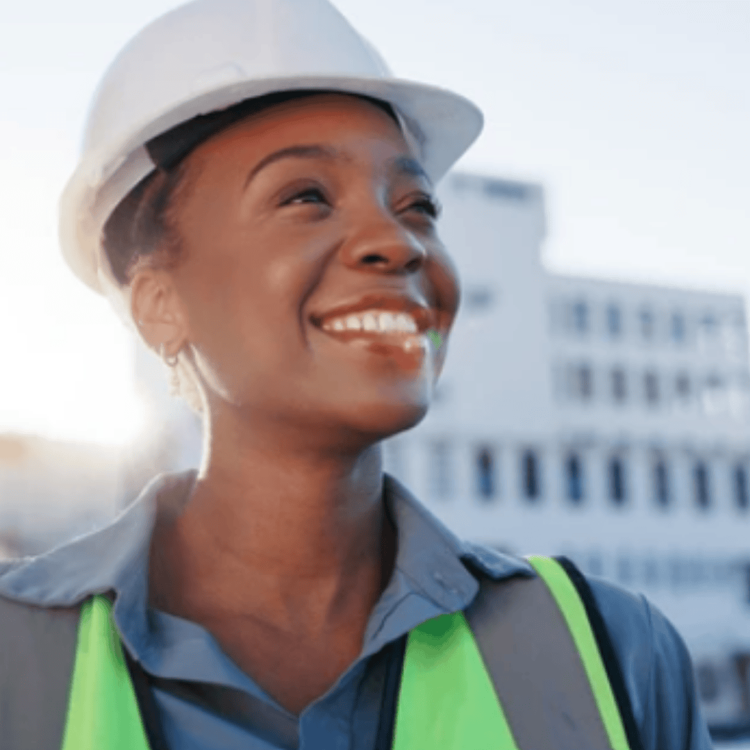 A woman wearing a white hard hat, safety vest, and collared shirt smiles outdoors with a blurred building in the background. The sun glows behind her, creating a bright and positive atmosphere free from brainrot.