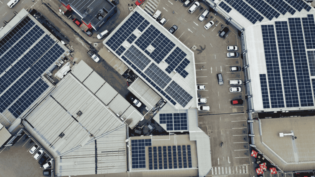 Aerial view of several large buildings with solar panels on their roofs and a parking lot filled with cars, highlighting new business opportunities in sustainable energy solutions.