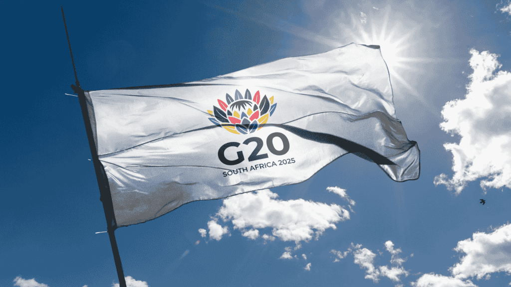 A white flag with a colorful flower emblem and the text G20 SOUTH AFRICA 2025 flutters against a sunny, blue sky, symbolizing new business opportunities on the global stage.