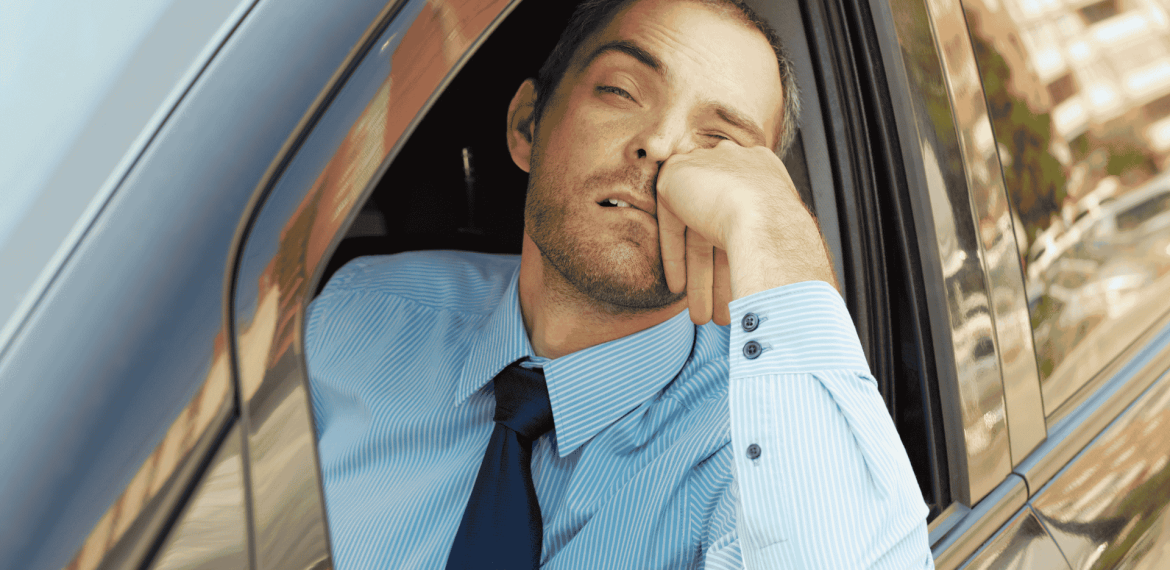 A man in a blue dress shirt and tie rests his head on his hand, looking tired and bored while sitting in a car with the window down, perhaps contemplating new business opportunities.