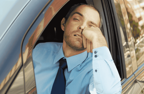 A man in a blue dress shirt and tie rests his head on his hand, looking tired and bored while sitting in a car with the window down, perhaps contemplating new business opportunities.