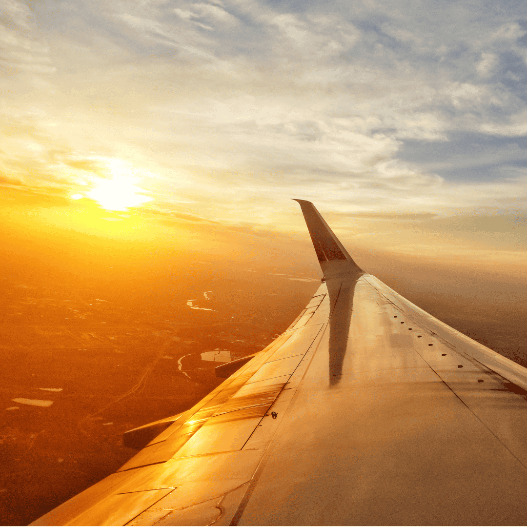 View from an airplane window showing the wing and engine in the foreground, with a golden sunset over scattered clouds—a reminder that new business opportunities await beyond every horizon.