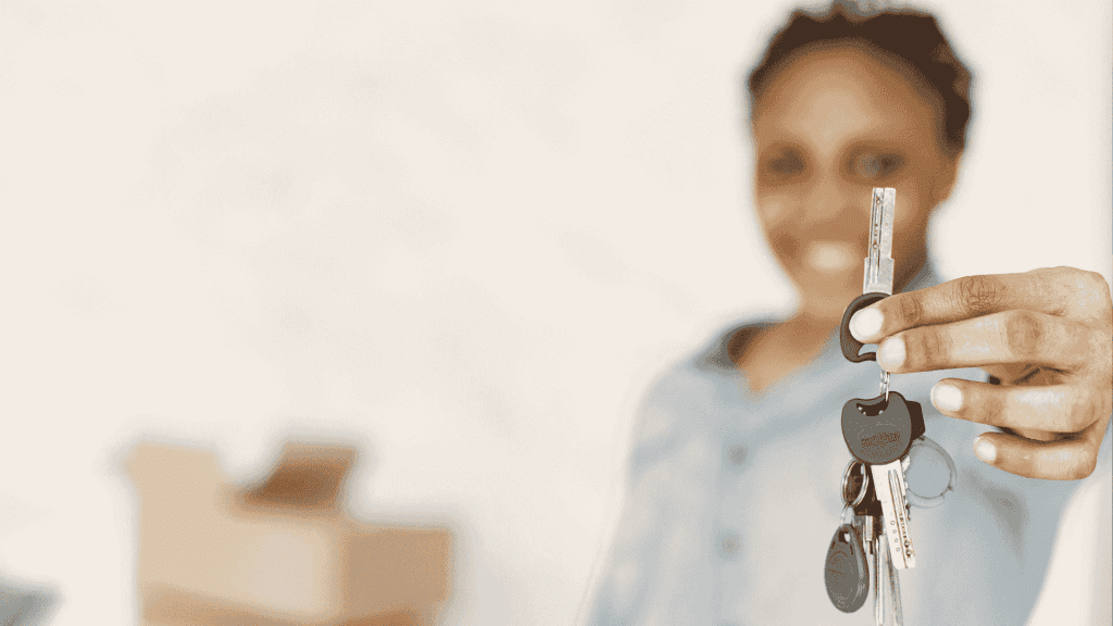 A person smiling and holding out a set of house keys, with moving boxes blurred in the background—symbolizing new beginnings and exciting business opportunities in real estate.