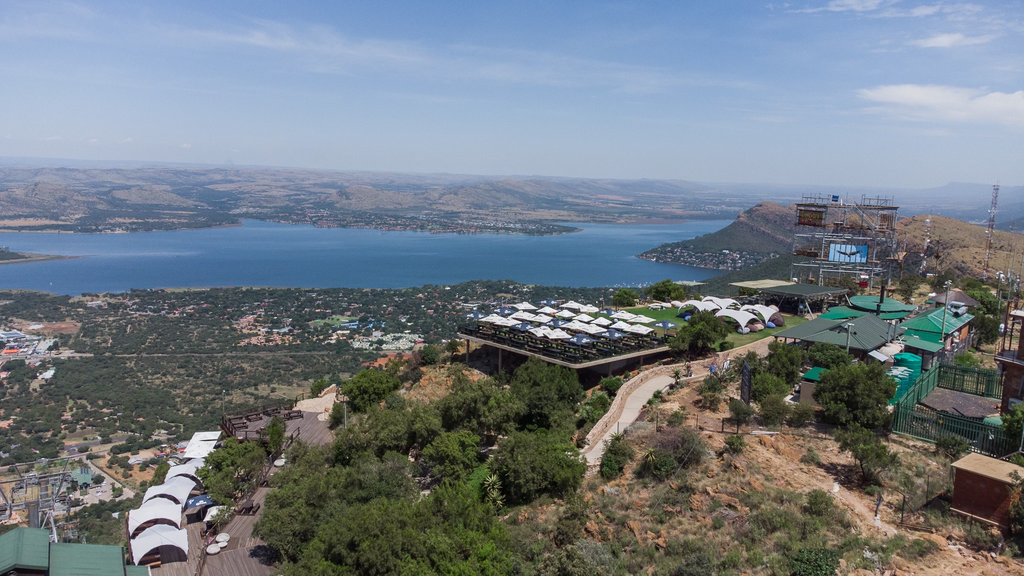Aerial view of a hilltop resort with terraces and pathways overlooking a large blue lake, surrounded by green vegetation and distant mountains under a clear sky—perfect for celebrating Heritage Day in nature’s embrace.