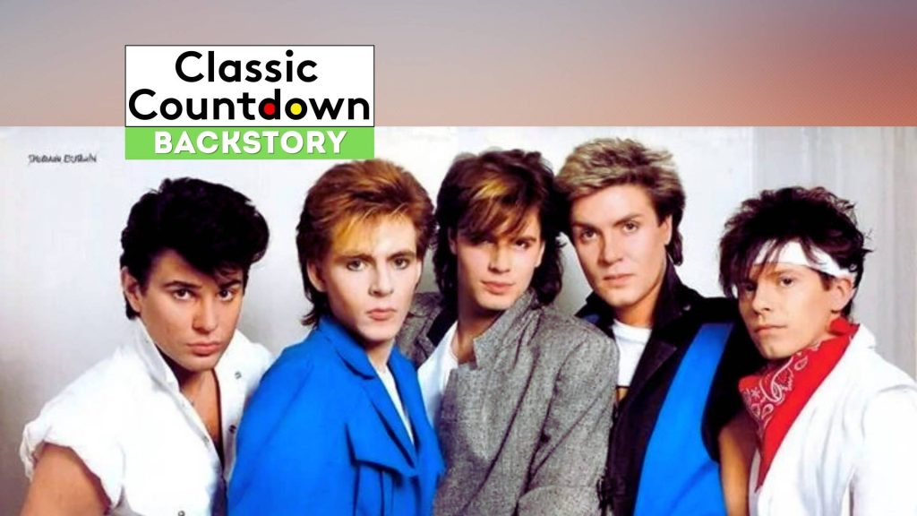 Five men with 1980s hairstyles and colorful outfits pose together against a light background. A banner at the top reads Classic Countdown Backstory, hinting at a nostalgic vibe reminiscent of hits like "Last Christmas.