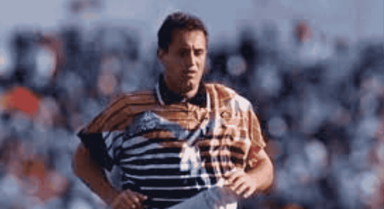 Mark McNulty, in a distinctive orange, black, and white striped jersey, is running on the field as blurred spectators watch from the background.