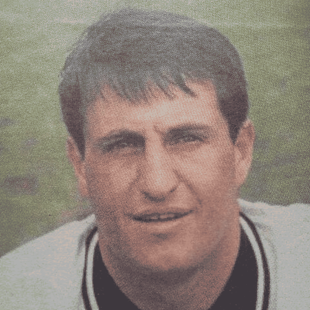 Mark McNulty, a man with short dark hair wearing a sports jersey, is outdoors with grass visible in the blurred background. He is looking slightly above the camera, his expression neutral.