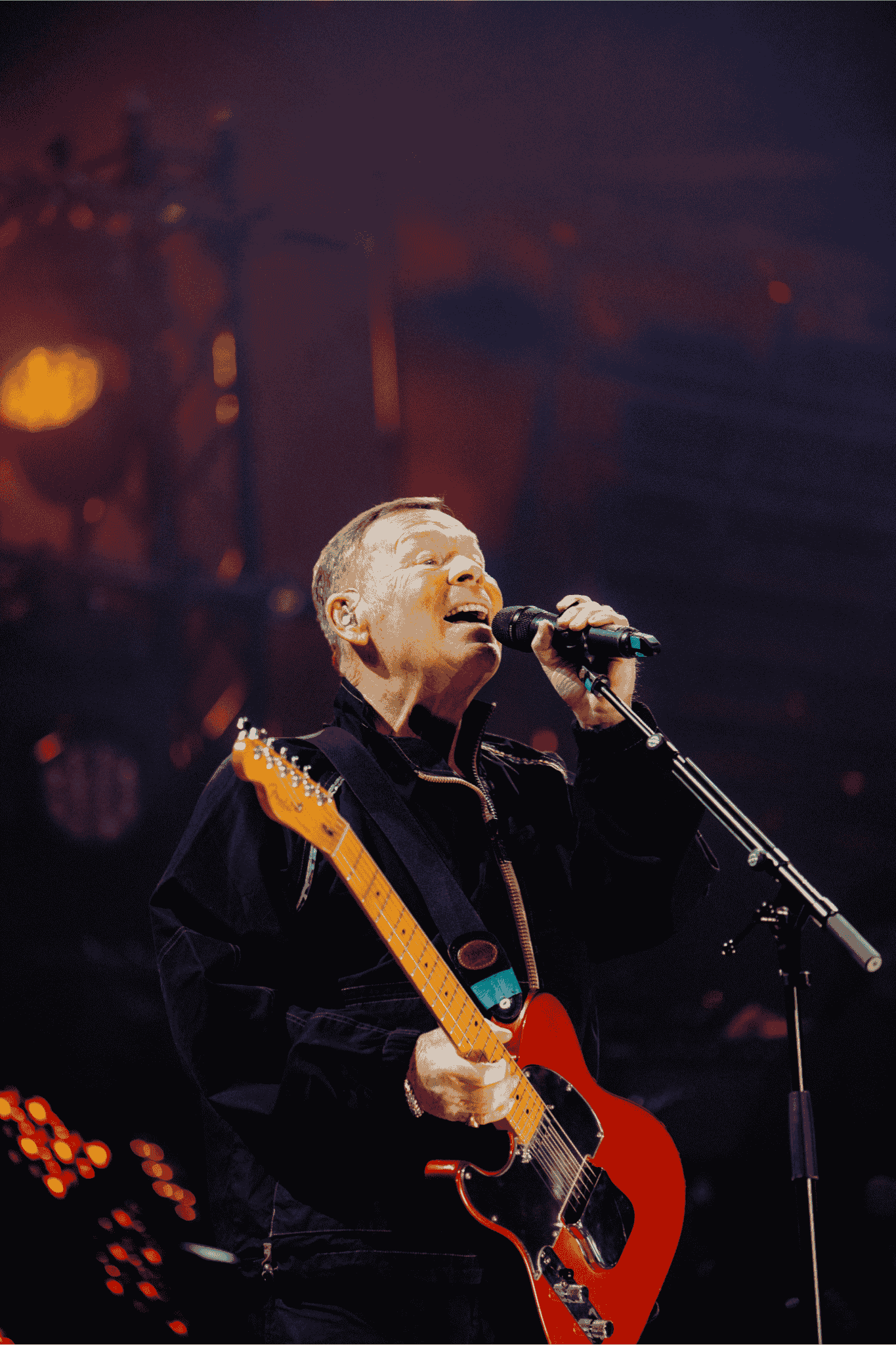 A musician wearing a dark outfit sings passionately into a microphone while playing an electric guitar on stage, under dramatic lighting, evoking the soulful energy of Miriam Makeba.