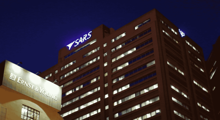 A nighttime view of two office buildings, one with a glowing ERNST & YOUNG sign and the other with a SARS sign near the top, their many lit windows shining like a Matric celebration against the dark sky.
