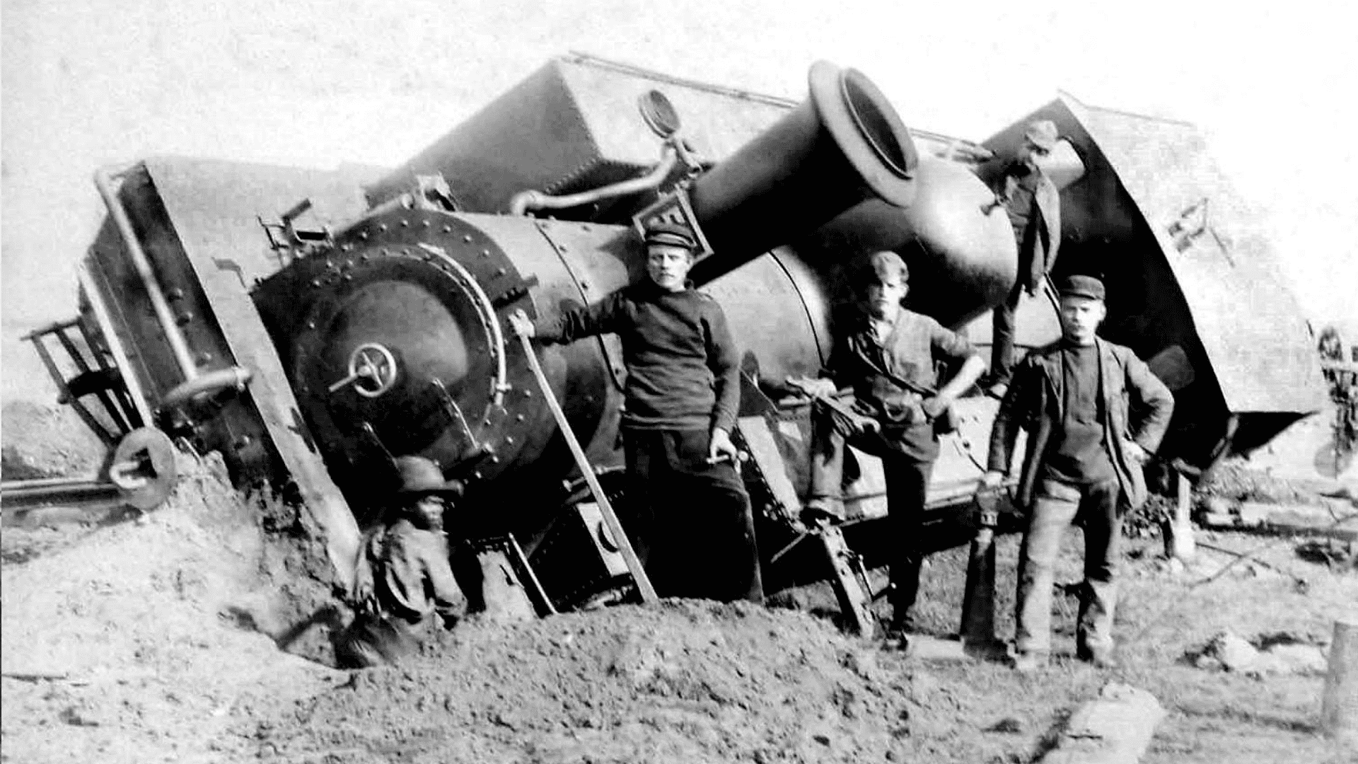 Three men in military uniforms stand next to an overturned steam locomotive, partially buried in dirt, with a young boy crouching nearby—a striking early 20th-century scene reminiscent of stories sung by icons like Miriam Makeba.
