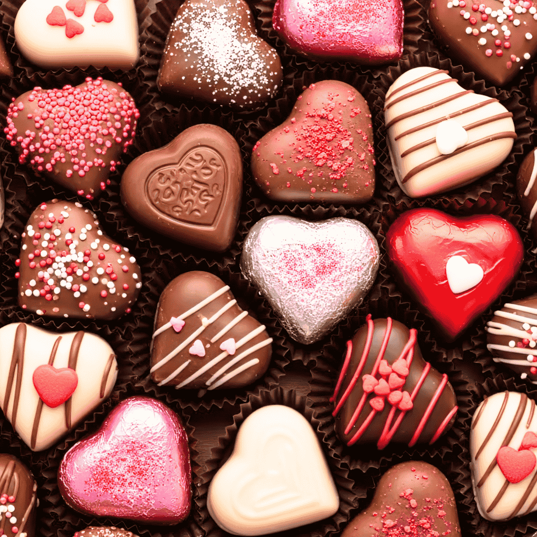 Assorted heart-shaped chocolates decorated with pink, white, and red icing—perfect for celebrating a Matric milestone—some topped with sprinkles and arranged closely together in paper cups.