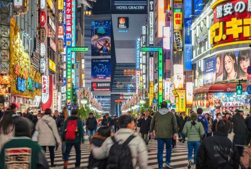 A busy city street in Tokyo at night, filled with people walking and crossing the road, surrounded by colorful neon signs—an exciting getaway for those who love urban travel vibes.
