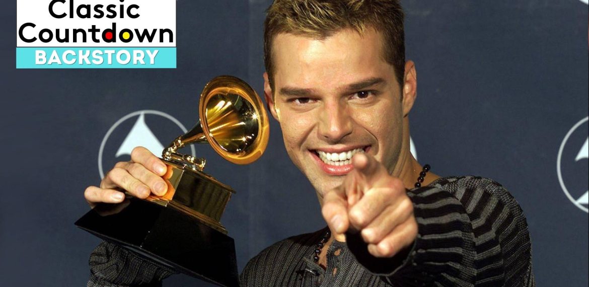 A smiling man holds up a Grammy award and points toward the camera. The background shows the Grammy logo, and a Classic Countdown Backstory graphic in the upper left corner highlights "Last Christmas.