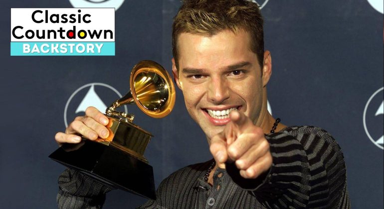 A smiling man holds up a Grammy award and points toward the camera. The background shows the Grammy logo, and a Classic Countdown Backstory graphic in the upper left corner highlights "Last Christmas.