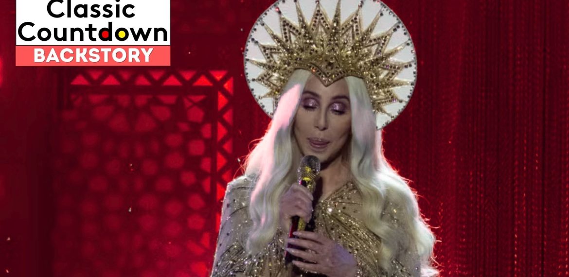 A person with long platinum-blonde hair, wearing a gold, ornate crown and sparkly gold outfit, sings "Last Christmas" into a microphone on stage with a red background. The text Classic Countdown Backstory is in the upper left corner.