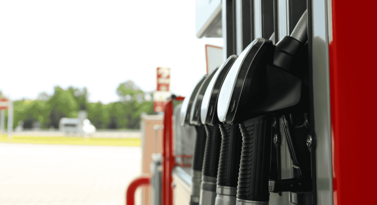 Close-up view of several black fuel pump handles at a gas station, with a blurred background showing trees and an empty forecourt—a striking scene reminiscent of a new show lineup waiting to debut.