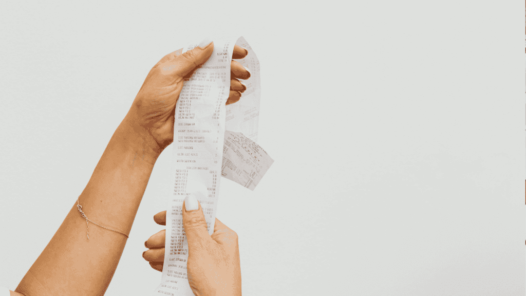 A person holding a long matric receipt with both hands against a plain white background. The receipt appears to have many items listed on it.