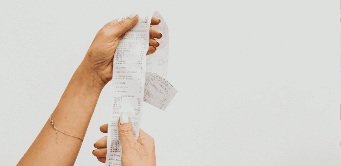 A person holding a long matric receipt with both hands against a plain white background. The receipt appears to have many items listed on it.