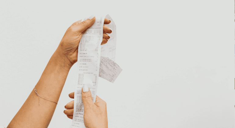 A person holding a long matric receipt with both hands against a plain white background. The receipt appears to have many items listed on it.