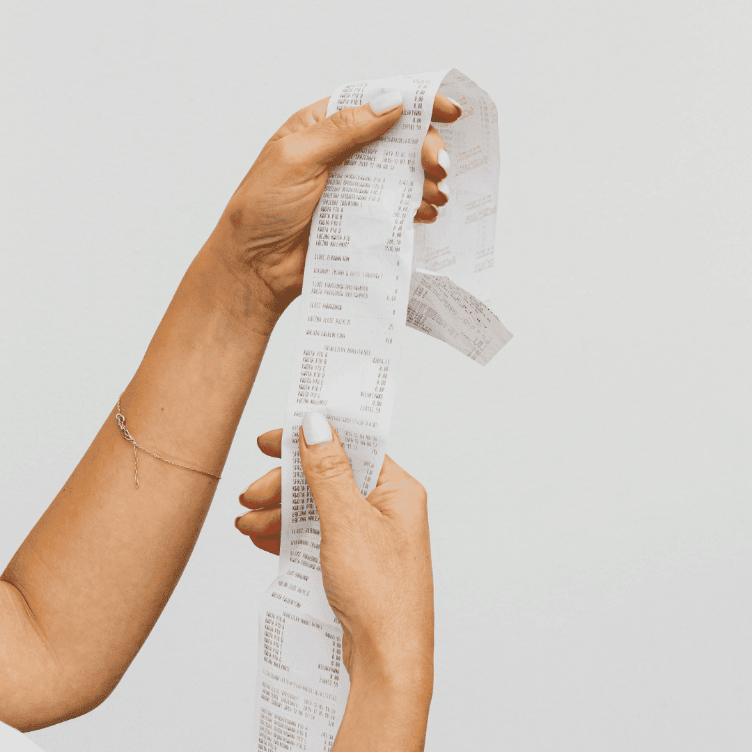 A person with light nail polish holds and examines a long, printed matric receipt with both hands against a plain white background.