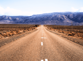A straight, empty road stretches into the distance through a dry, brown landscape with mountains in the background under a partly cloudy sky, evoking the feeling of setting out on a new journey after completing matric.
