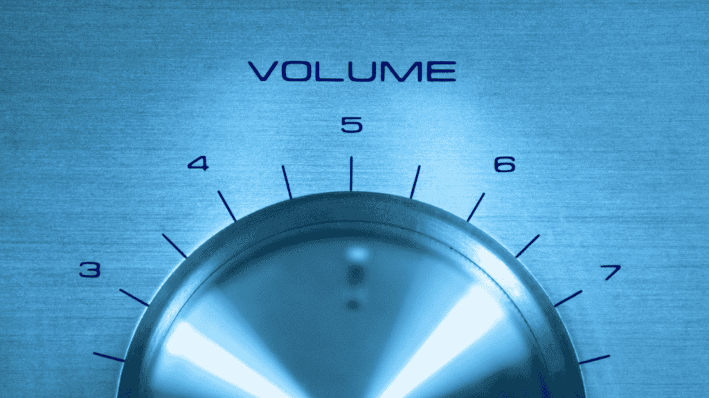 A close-up of a metallic volume control knob set between levels 5 and 6, with numbers 4 to 7 visible above the knob and "VOLUME" printed above in blue text. The blue-tinted image channels the early energy of a hot 1027 breakfast show.