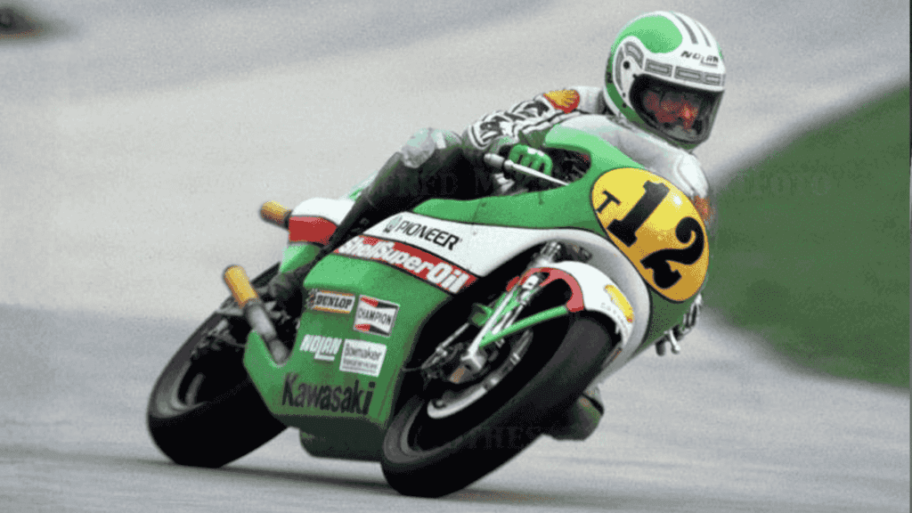 Mark Andrews, a motorcycle racer wearing a green and white suit and helmet, leans into a turn on his green Kawasaki bike numbered 12 during a race on a paved track.