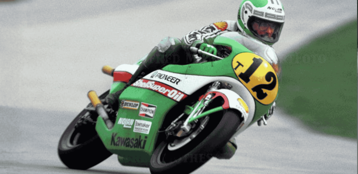 Mark Andrews, a motorcycle racer wearing a green and white suit and helmet, leans into a turn on his green Kawasaki bike numbered 12 during a race on a paved track.