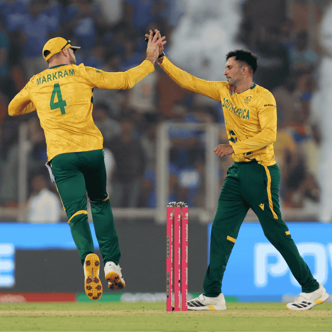 Two South African cricket players in yellow and green uniforms celebrate by high-fiving during a match, bringing energy reminiscent of a Hot 1027 Breakfast. The player on the left, wearing number 4, jumps in the air as the other cheers from the ground.