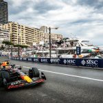 A Formula 1 car races along a street circuit by the waterfront, with tall buildings, yachts, and spectators in the background under a cloudy sky. MSC Cruises banners line the track, capturing the thrill of travel and a high-speed getaway.