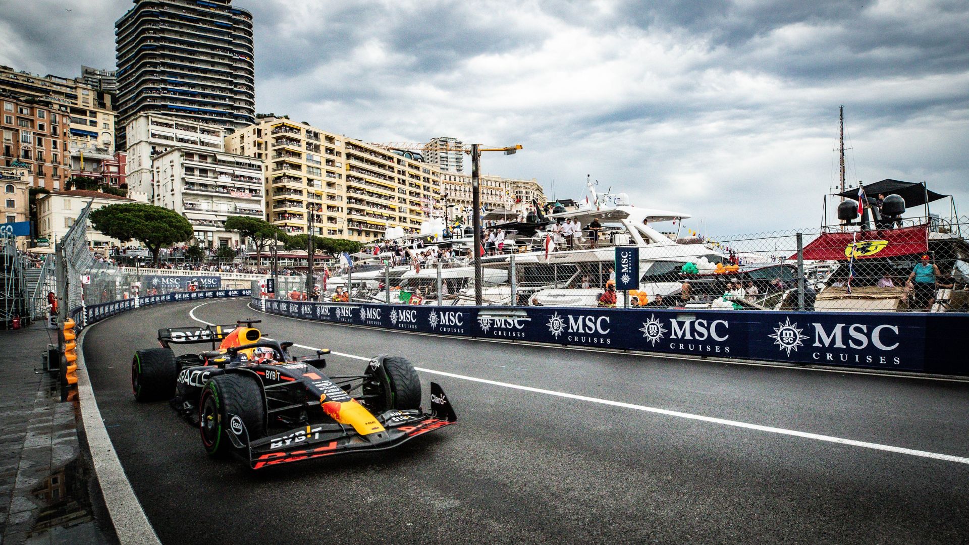 A Formula 1 car races along a street circuit by the waterfront, with tall buildings, yachts, and spectators in the background under a cloudy sky. MSC Cruises banners line the track, capturing the thrill of travel and a high-speed getaway.